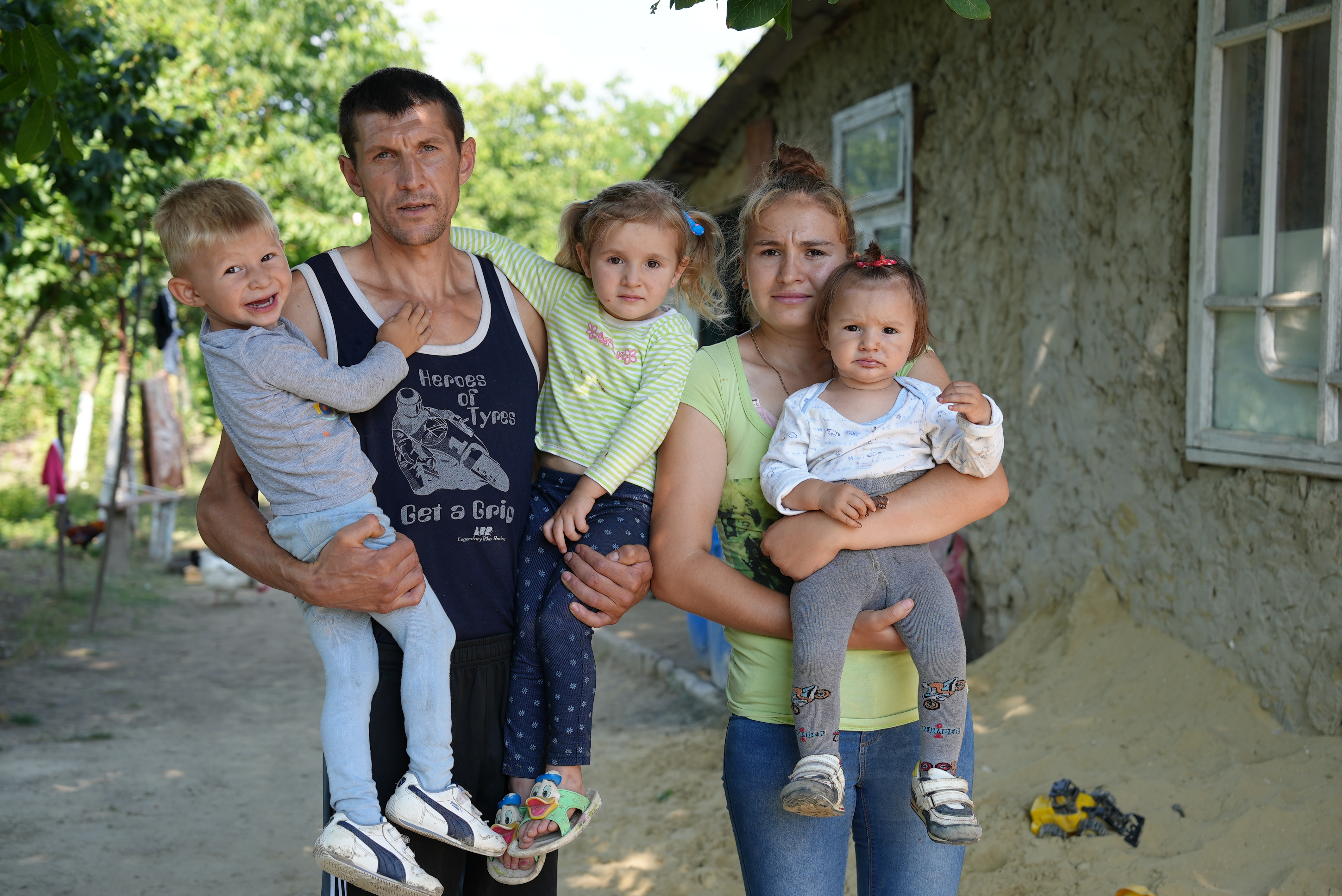 A father holds a little child as he stands next to his wife who holds two babies in front of their porch in Moldova