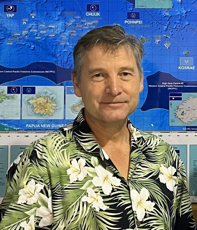 A man in a colourful shirt stands against a bright blue background