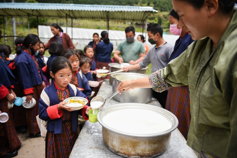 A person in a green dress serves a young child with a bowl