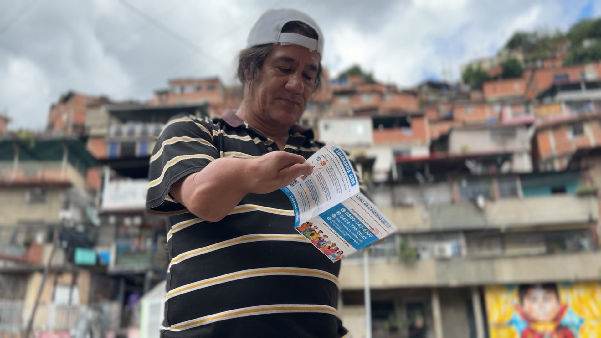 A man in a striped shirt and a backwards cap with a disability peruses through a pamphlet