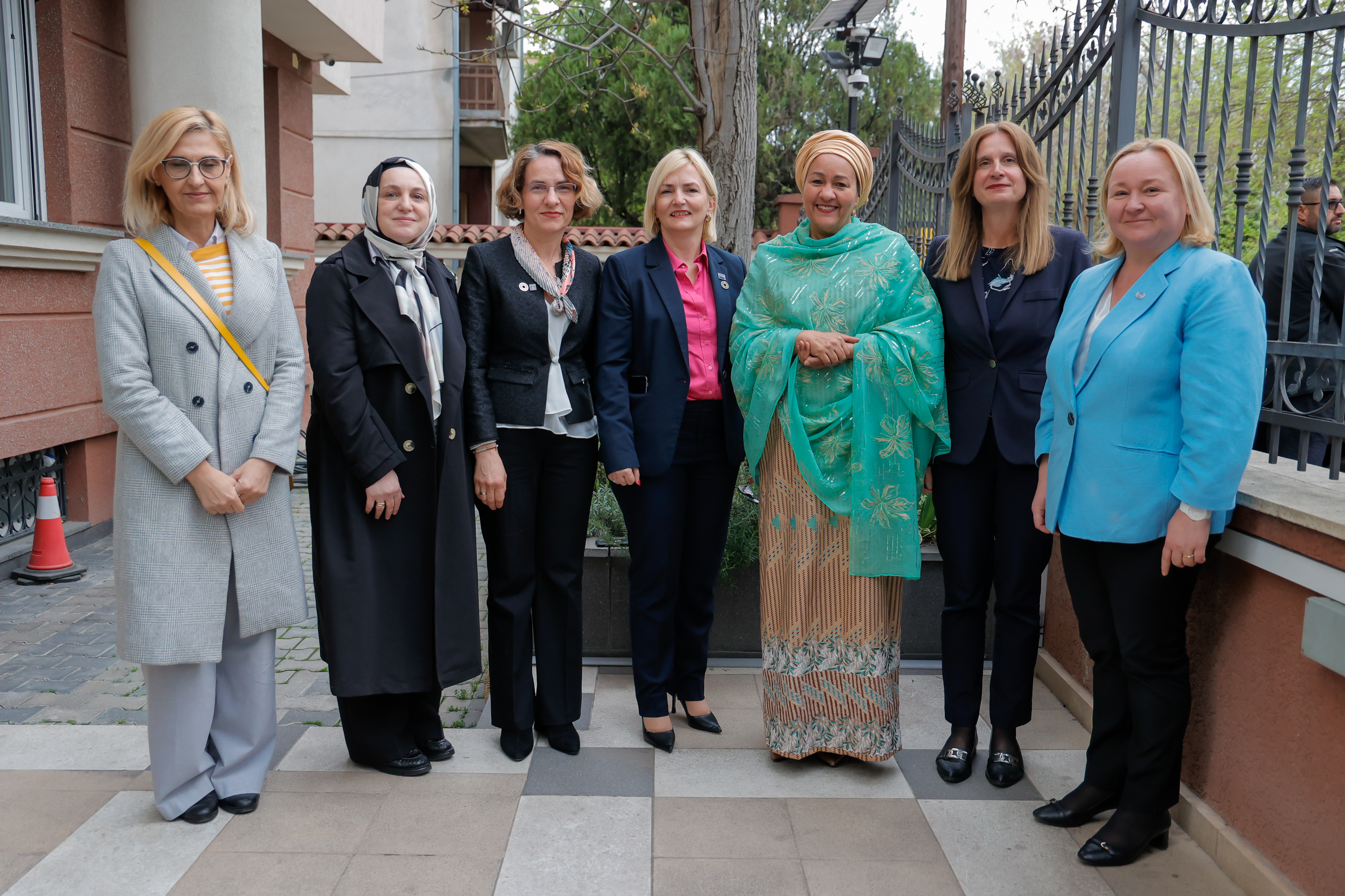 A group of seven women, most of them in suits stand in a row and smile.