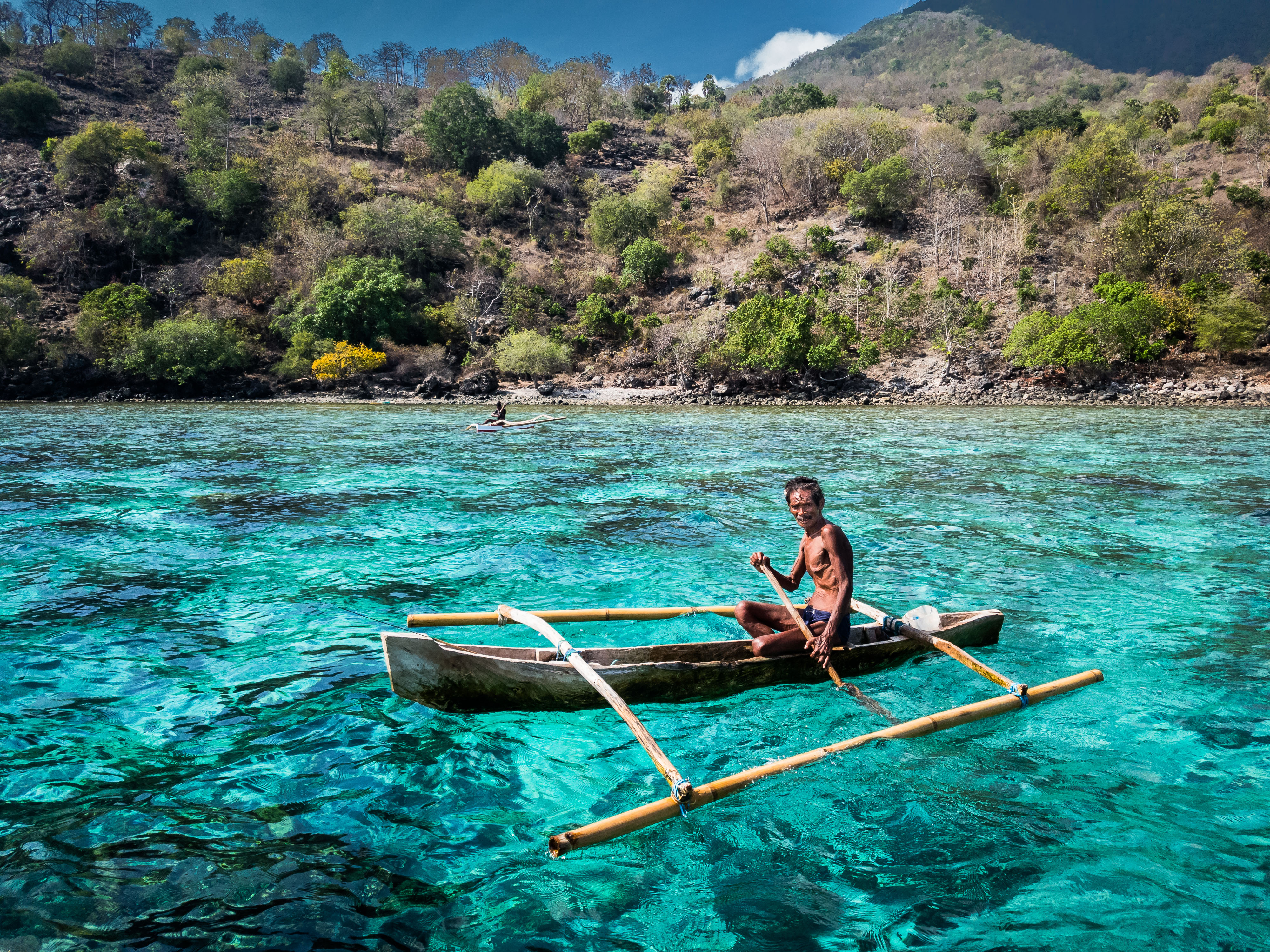 A man in a makeshift boat paddles through a blue lagoon in Indonesia