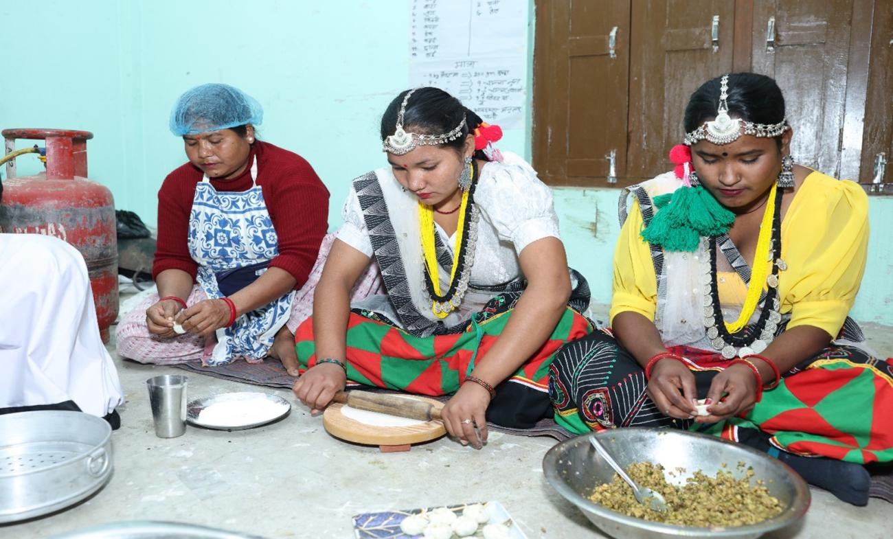 A group of women are sitting on the floor together cooking.