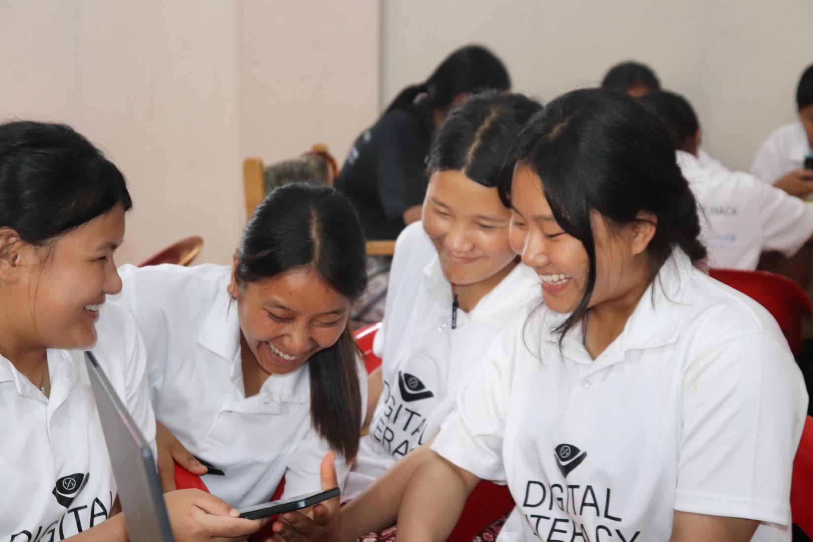 Four girls discussing and laughing while one holds a phone in her hand