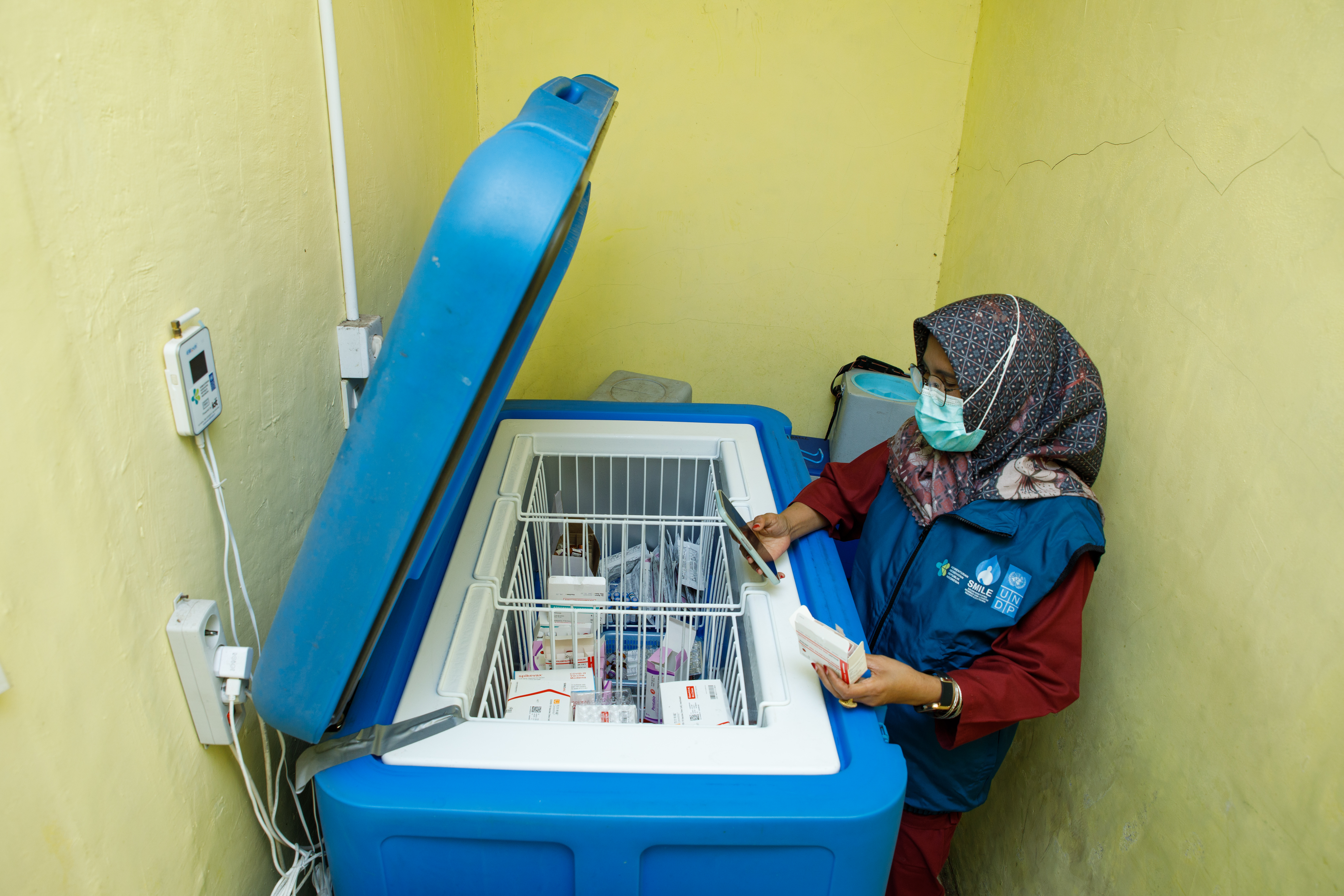 A female health worker in Indonesia looks at a container filled with vaccines and medical supplies. 