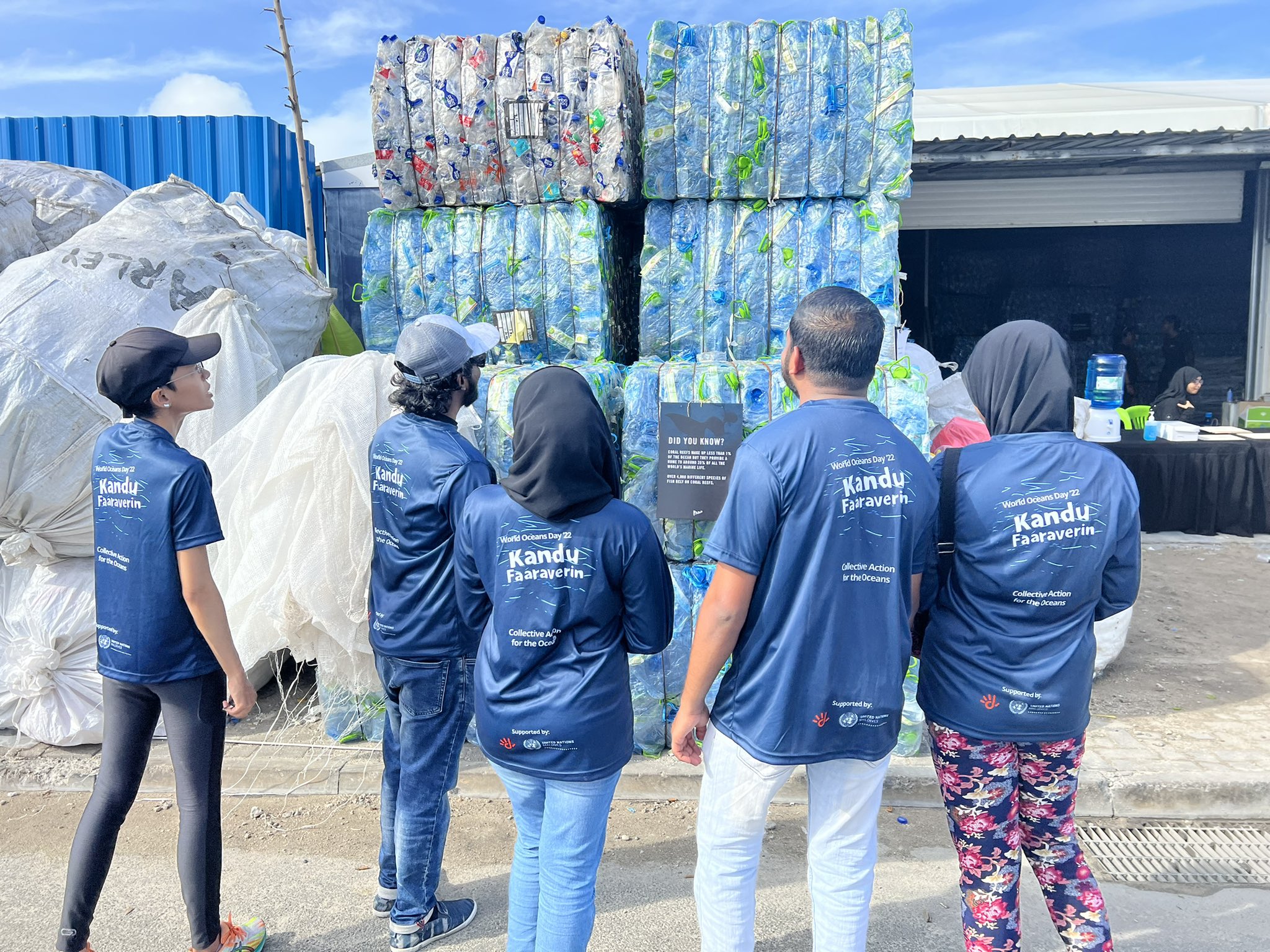 group of people with their backs turned stand looking at crates of plastic 