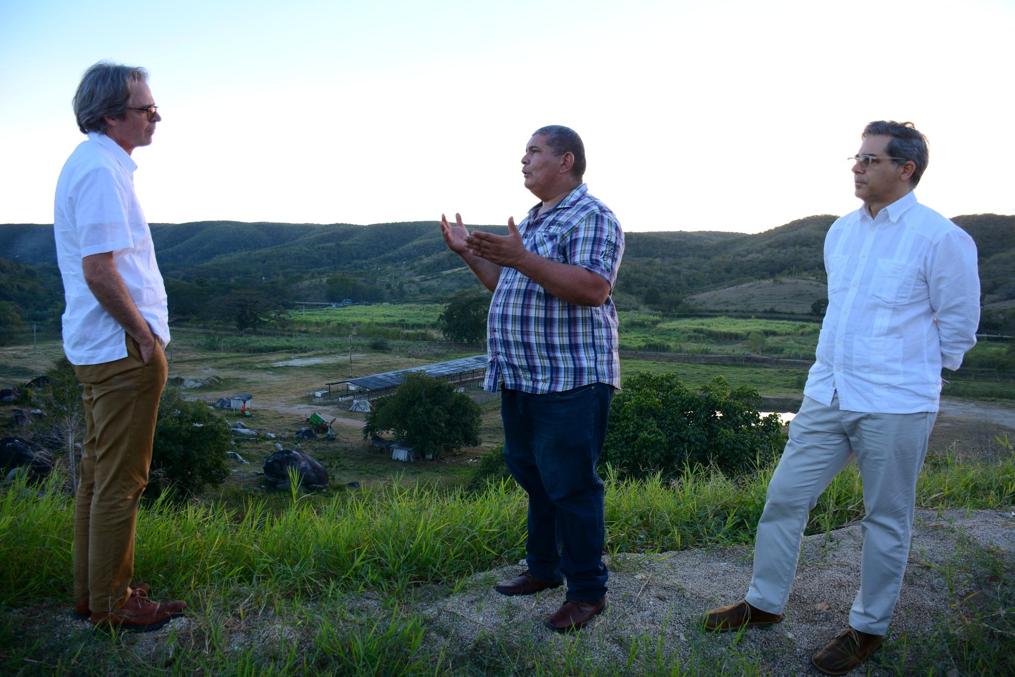three men stand outside in a rural landscape 