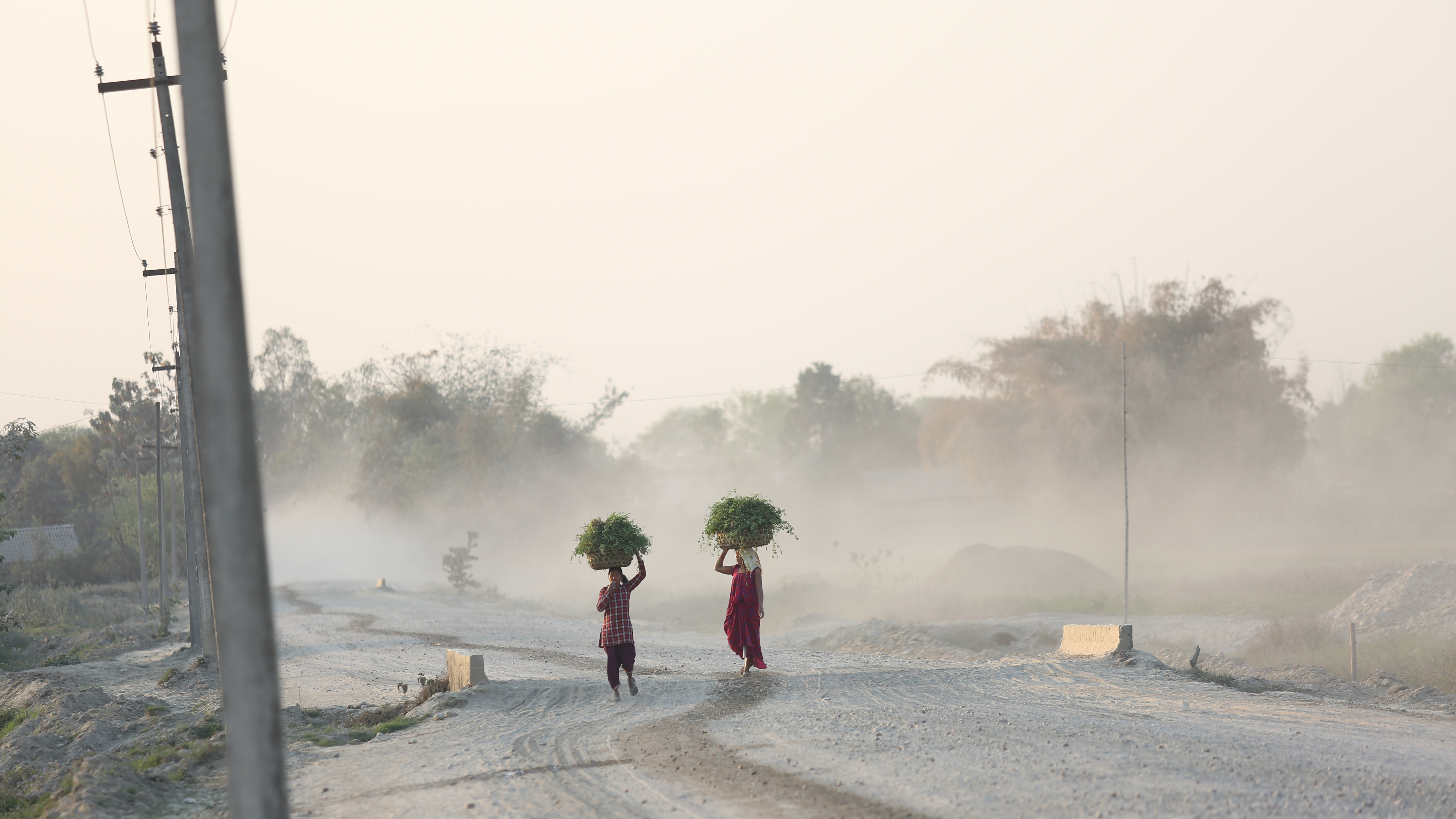 women walking down a road holding baskets of grass 