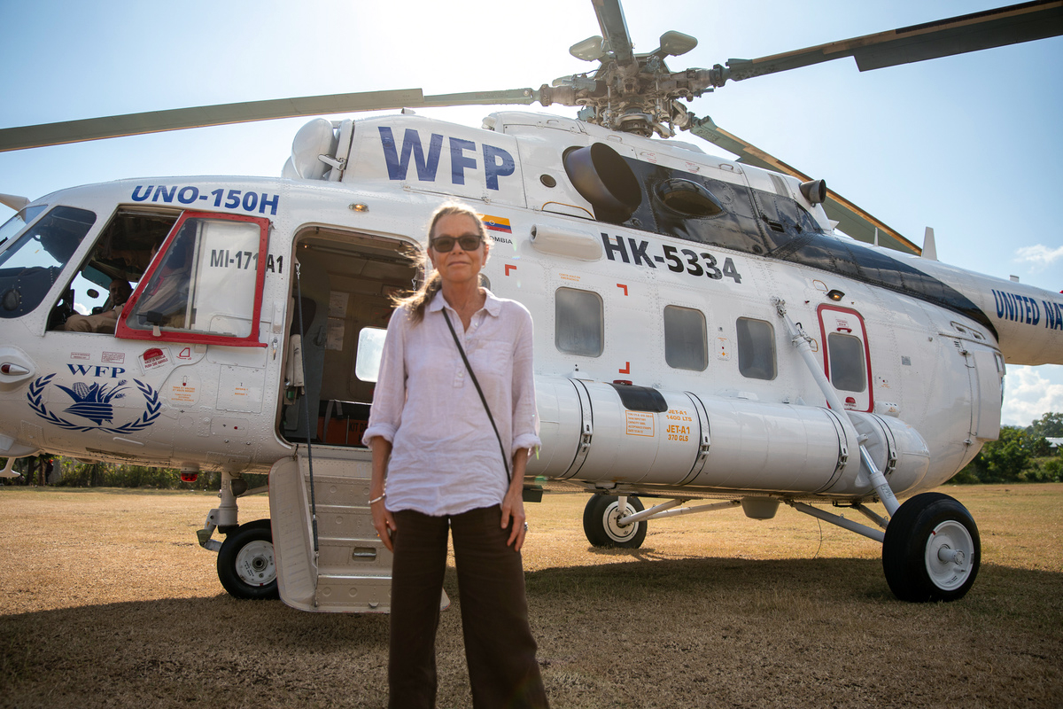 Women in white shirt stands in front of WFP helicopter.