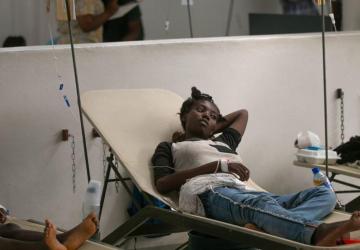 A woman lays on a cot near medical equipment. 