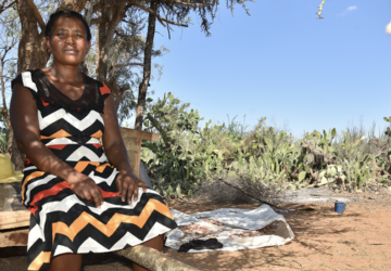 A woman sits near trees on a sunny day. 
