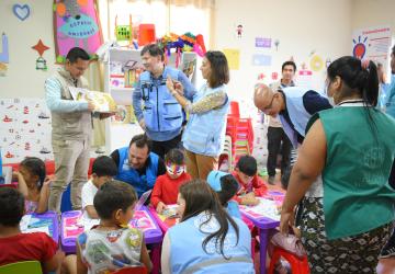 Women stands in a classroom with children taking a photo of a book 