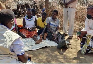 women kneels down speaking to a group of people on the ground 