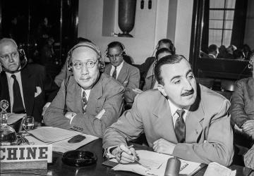 black and white photo of two men sitting at a desk with microphones 