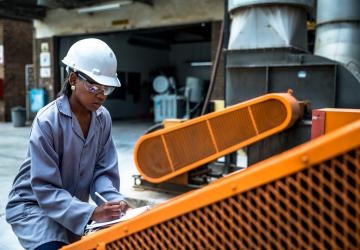 Women in hard hat kneels down to work on machinery 