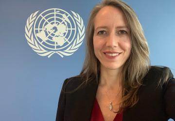 women smiles in front of a wall with the UN flag 