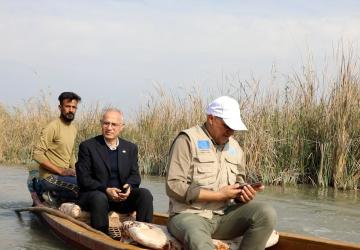 three men sit in a boat going down a marsh river in Iraq 