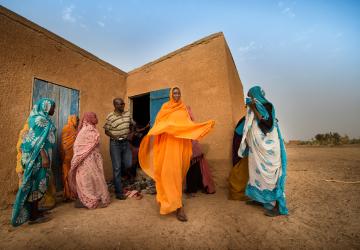 People in colourful clothes stand outside a building 