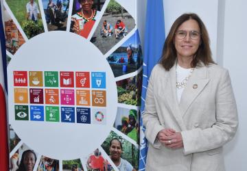 woman in beige suit stands next to the SDG logo 
