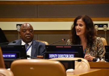 man in dark suit sits next to woman with long dark hair at panel event 