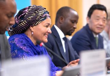 woman in blue top and dark head scarf smiles while sitting alongside other people at panel discussion 