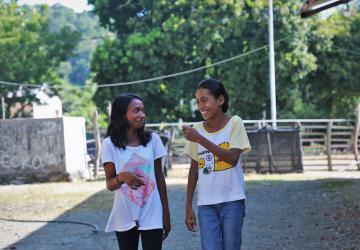 Two young girls speak to each other outside with trees in the background 