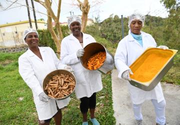 three women in white coats hold pans with food 