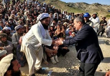 man in dark suit shakes hands with man in white robes 