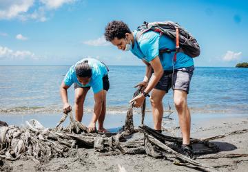 two people in blue t-shirts bend down to collect litter from the beach 