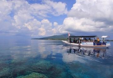 A small white boat with people sails over crystal blue waters in Indonesia