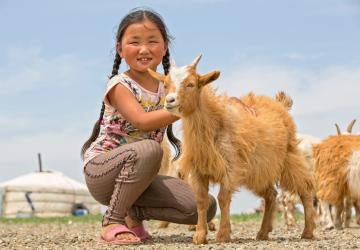 young girl bends down next to a goat