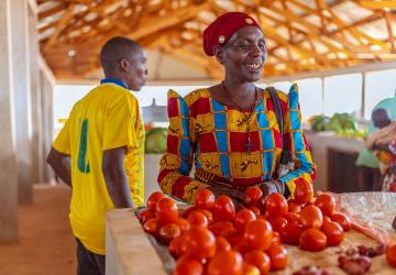 woman stands behind her tomato stand at market 