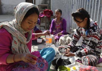 group of people sit down on the ground working with crafts and textiles 