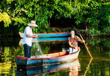 two people on a wooden rowing boat with trees behind them 