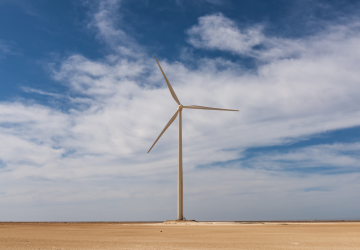 a wind turbine in a field against cloudy blue sky 