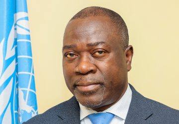 man in dark suit and blue ties stands in front of UN flag 