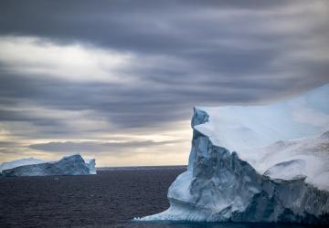 two mountains of ice float in the Antarctic sea against cloudy sky