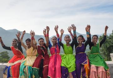 women in colourful saris raise their arms in the air and smile to the camera