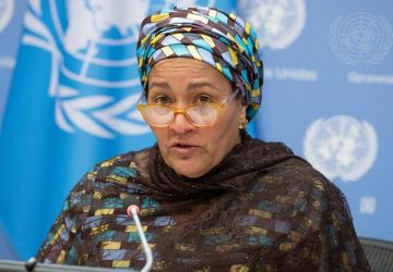 woman in colourful headscarf speaks into microphone against blue background