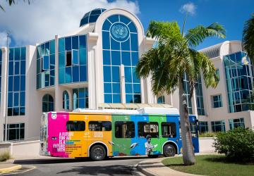 A multi-coloured bus standing in front a tall blue building (the UN in Barbados).
