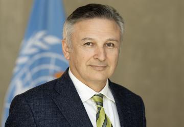 RC Rasul Baghirov, wears a dark suit and yellow and black striped tie and stands in front of a UN flag