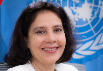 RC Gita sits in front of the UN flag. She is wearing a white top