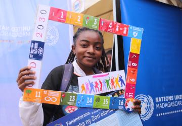 A young girl holds up a banner of the SDGs, she is smiling