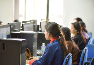 A schoolgirl in Bhutan, dressed in blue clothes, sits at a desk browsing a computer