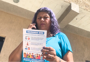 A woman in a blue shirt with purple hair calls someone on her mobile phone while reading a pamphlet