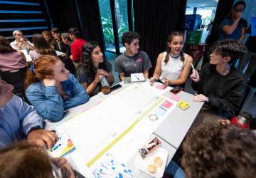 A group of young people seated around a table, engaged in a discussion