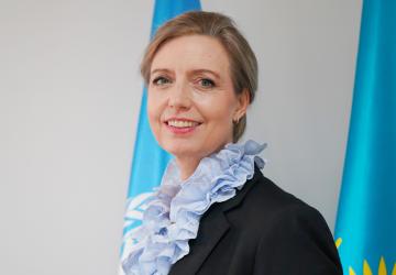 A headshot of a woman in black suit and blue scarf