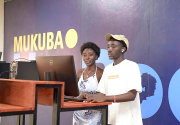 Two people in front of a computer with a colourful background behind them