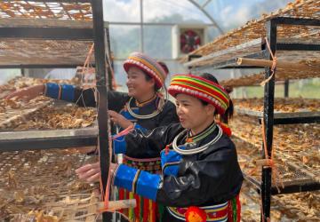 Two women in traiditional colourfull dress in an outdoor space are working on drying produce on drying 