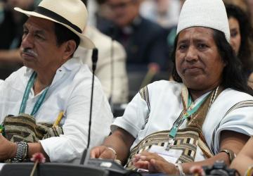 A group of people in traditional dress are seated and looking forward in an indoor conference hall